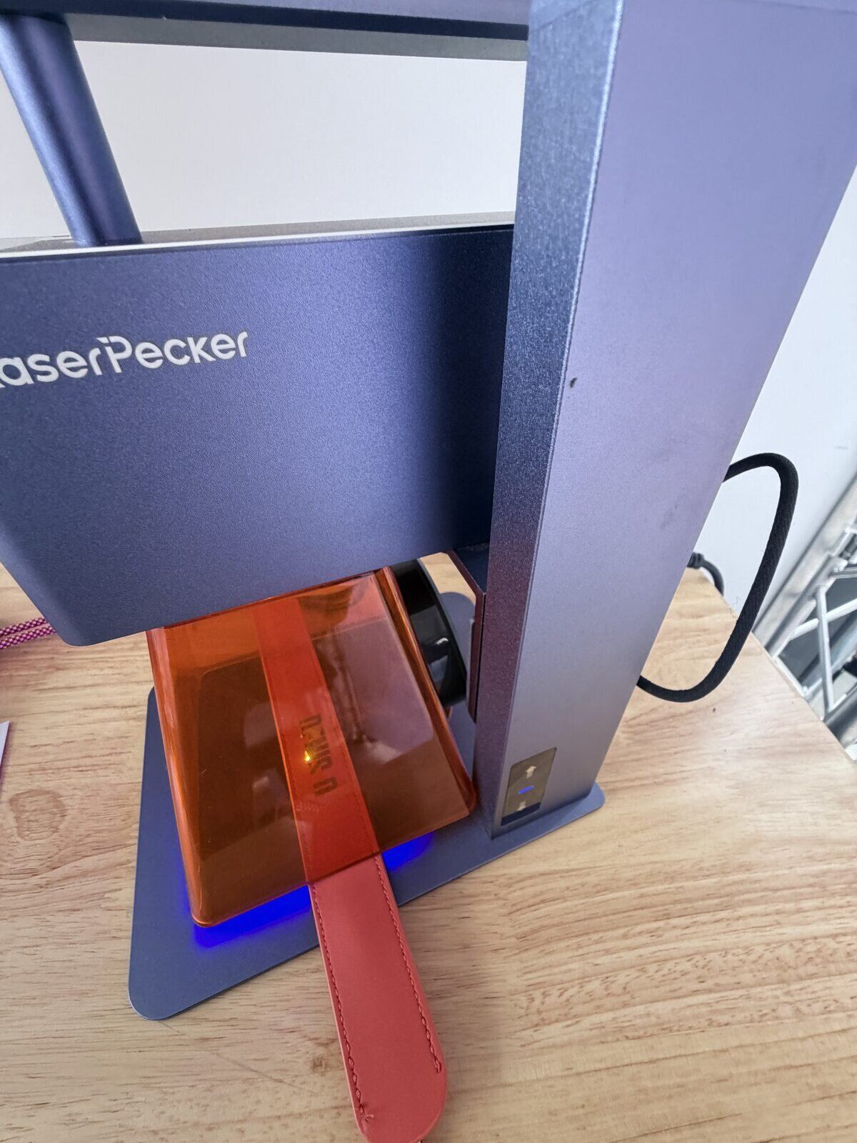 Compact laser engraver personalizing a red leather strap at an event station